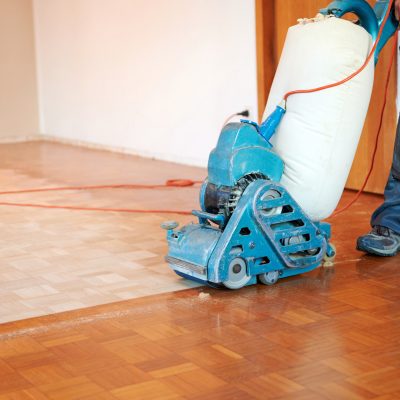 Worker polishing parquet floor with grinding machine